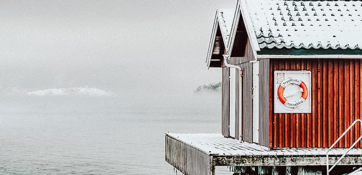 en rød hytte ved vannet med redningsbøye på veggen