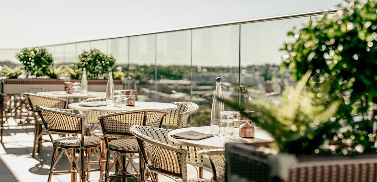 Utendørs takterrasse med stilfulle møbler, glassrekkverk, og innebygde blomsterpotter, solfylt omgivelse.