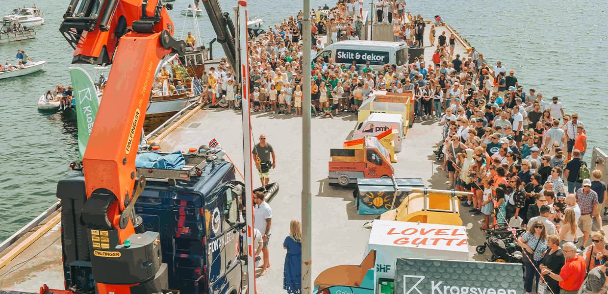 En travel scene med en mengde mennesker og små tilpassede kjøretøy som gjør seg klare til et spektakulært arrangement ved en havneområde.