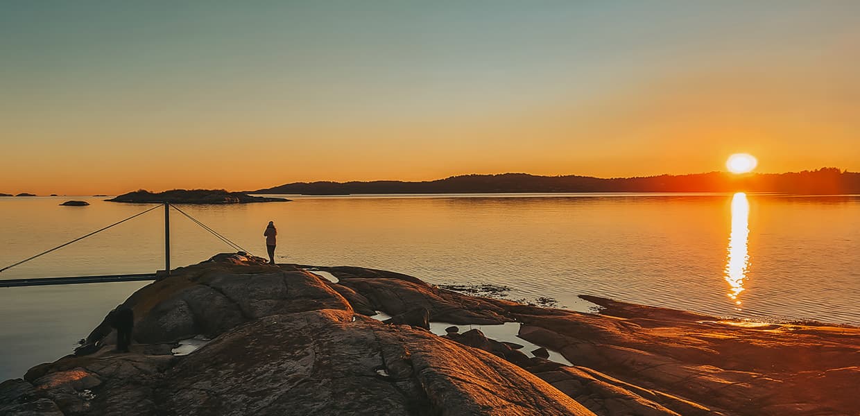 person på svaberg i solnedgang ved havet