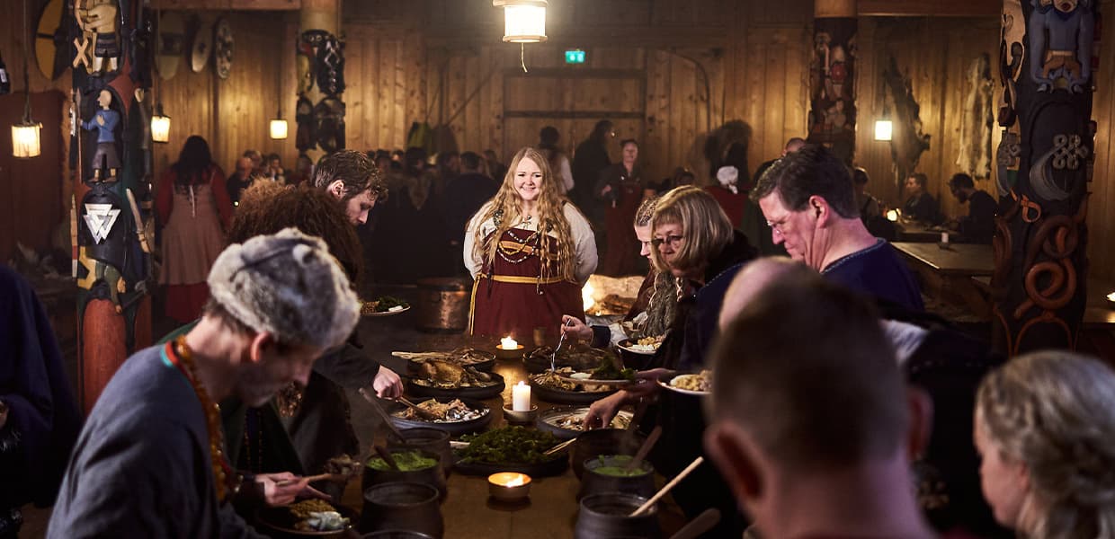 Måltid i Gildehallen: Mennesker samlet rundt et bord med stearinlys, kledd i historiske drakter.