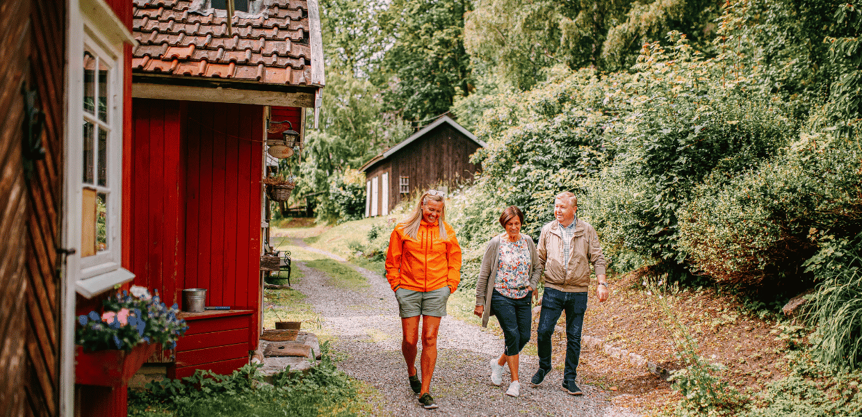 tre personer går forbi et rødt trehus